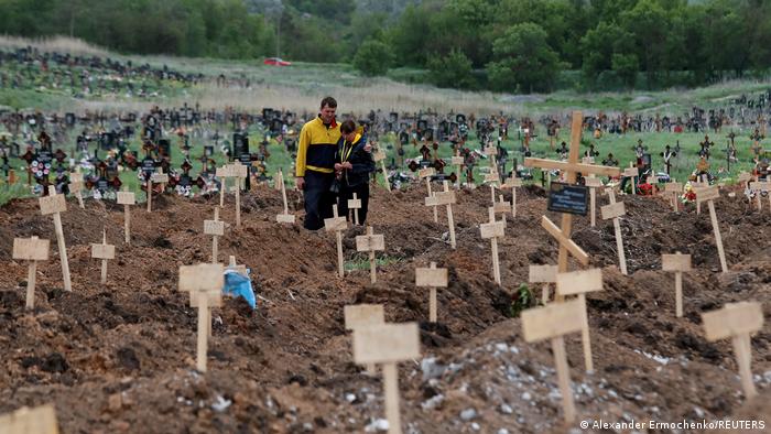 Двоє мешканців Маріуполя на цвинтарі зі свіжими могилами у місті Старий Крим на околиці міста Маріуполь, 22 травня 2022 року.