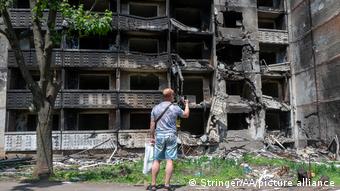 Чоловік фотографує на смартфон зруйнований багатоквартирний будинок у Харкові
