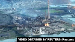 На этом кадре с видео, которое недатировано, но было обнародовано 15 мая 2022, видно падение на территорию завода «Азовсталь» большого количества ярких зажигательных снарядов (справа в воздухе) во время вторжения России в Украину.  Мариуполь