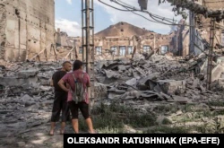 Местные жители смотрят на разрушенные здания в Лисичанске после тяжелых боев в Луганской области, Украина, 18 июня 2022 года, в пяти километрах северо-восточнее Северодонецка