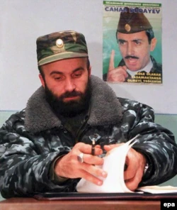 Шамиль Басаев рассматривает документы, сидя рядом с плакатом первого президента Чечни Джохара Дудаева в Грозном, 21 января 2001 года