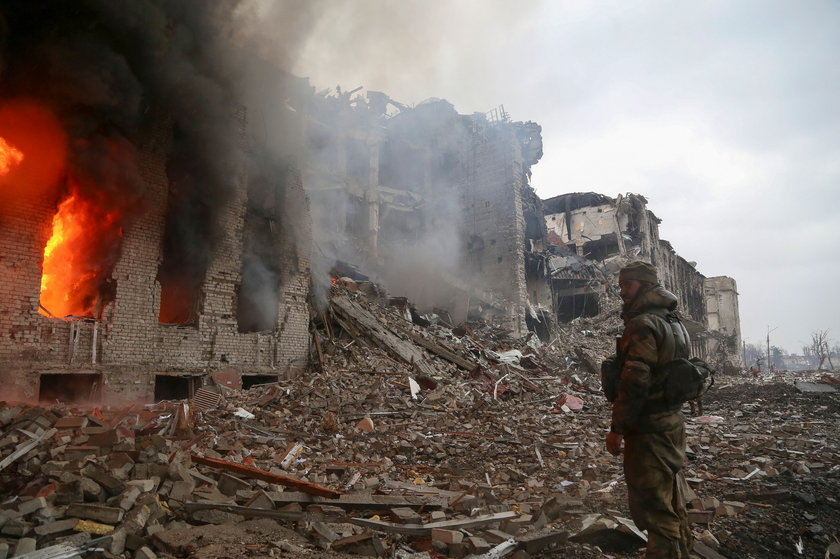 Російський солдат без емоцій перед зруйнованим і палаючим будинком у Маріуполі