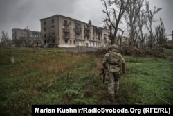 Военный ВСУ идет к разбитым зданиям в Соледаре